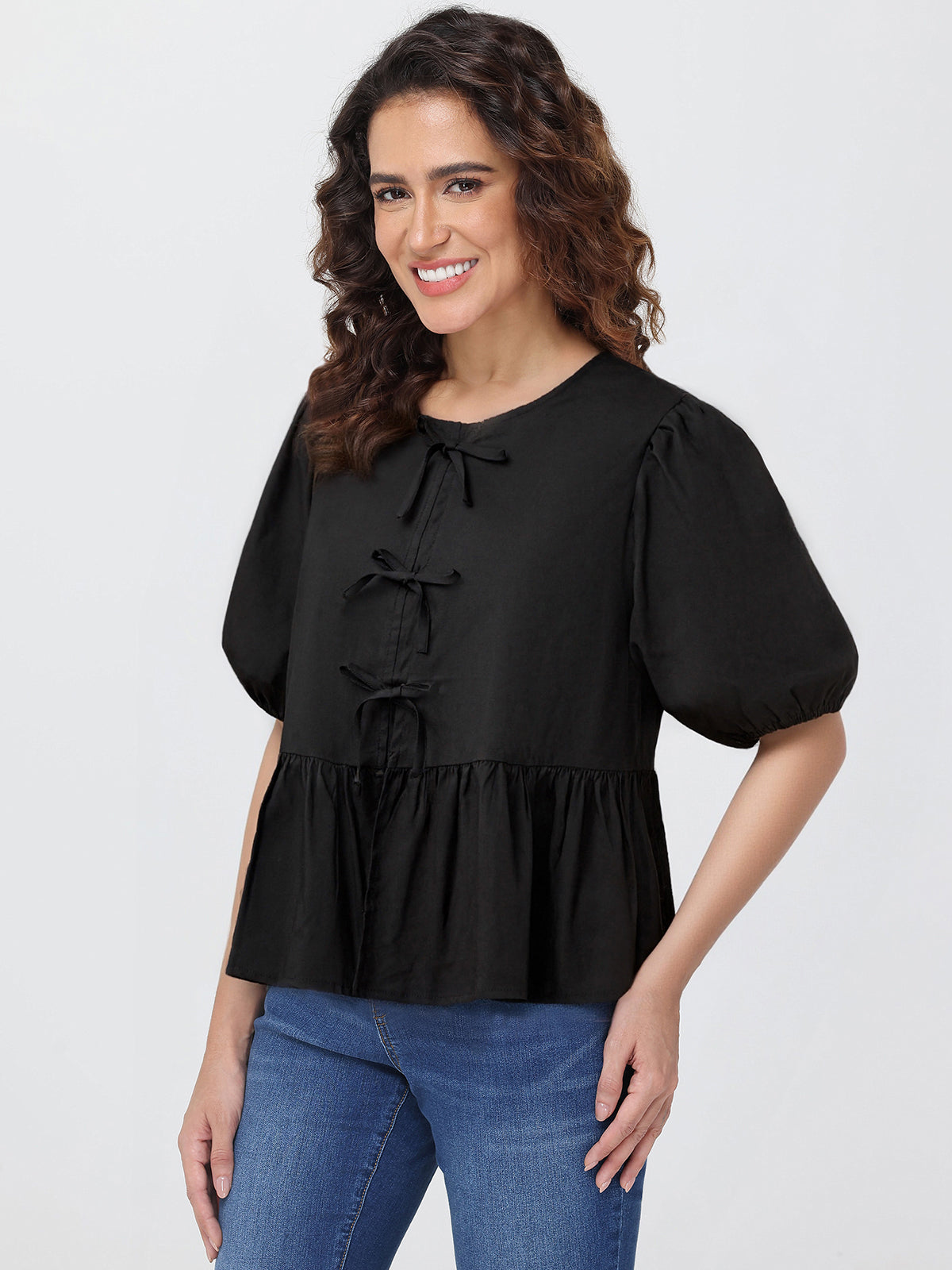 Woman wearing a black blouse with puff sleeves and blue jeans on a white background