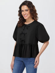 Woman wearing a black blouse with puff sleeves and blue jeans on a white background