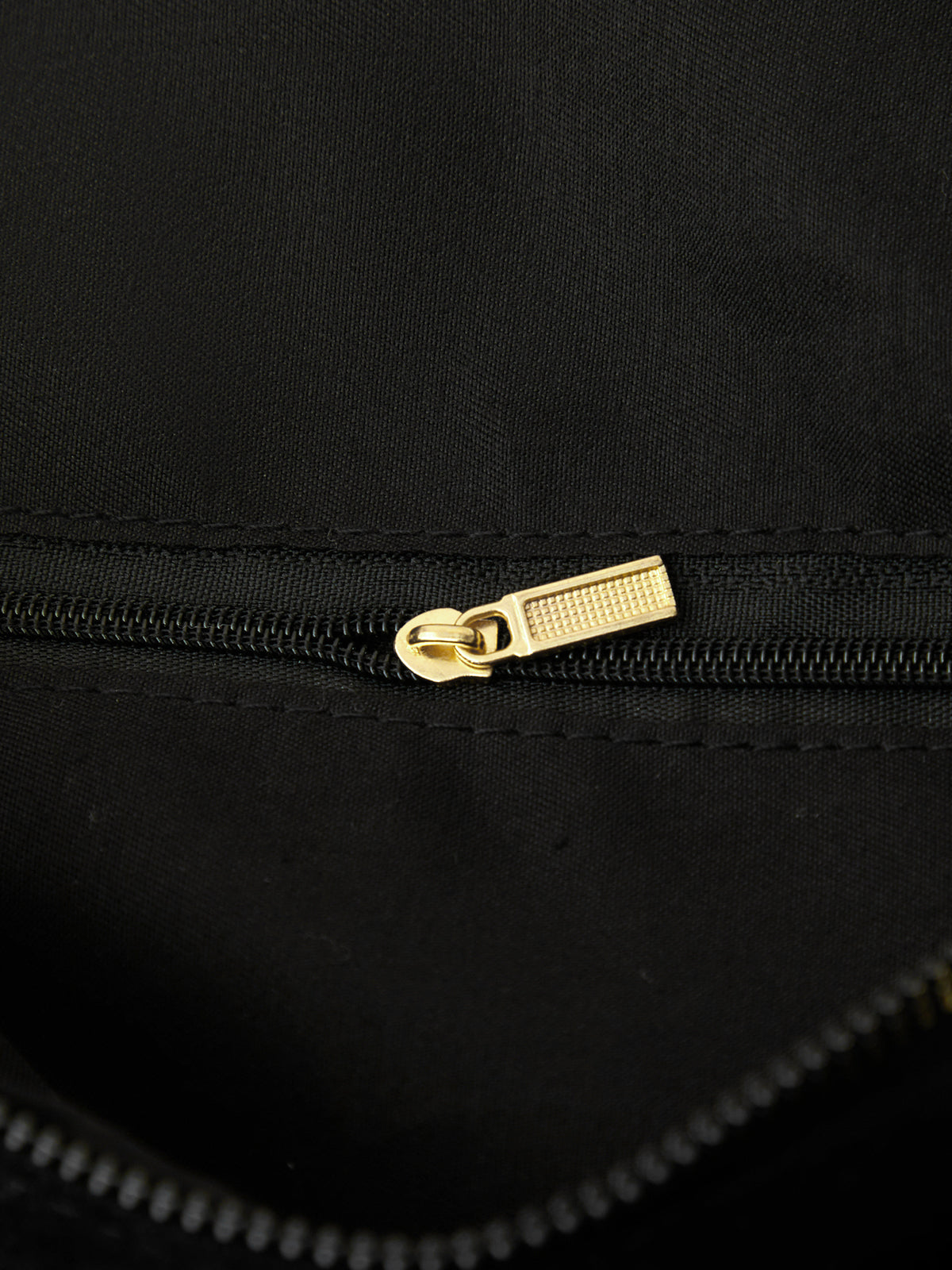 Close-up of a black bag with a gold zipper pull.