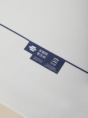 A close-up of a dark blue product label with white text and logos, attached to a thin dark blue line on a plain white background.
