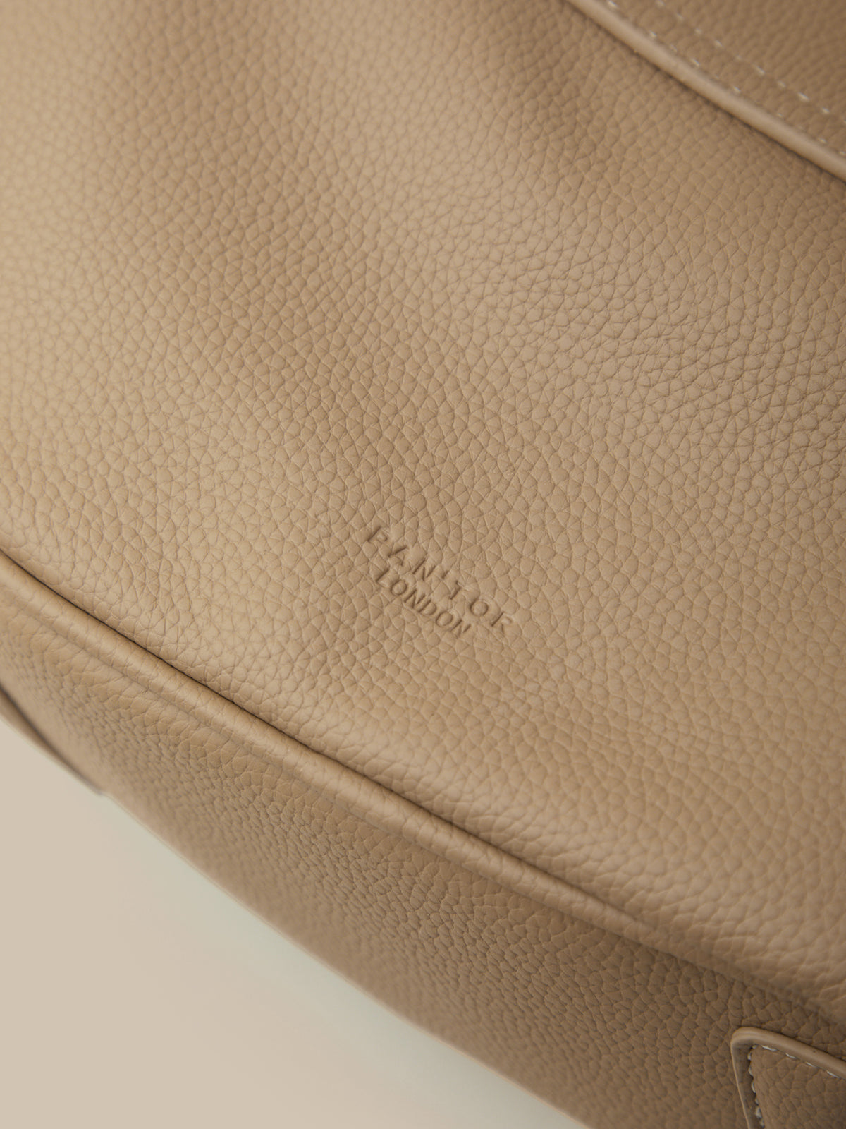 Close-up of a beige leather bag with 'Farrukh London' branding.