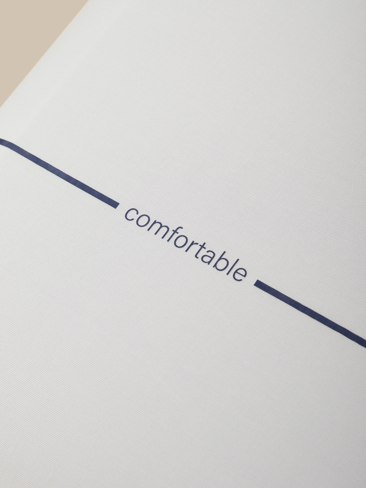A close-up of a pillow with the word 'comfortable' printed in dark navy blue lowercase text, centered between two short navy blue horizontal lines.