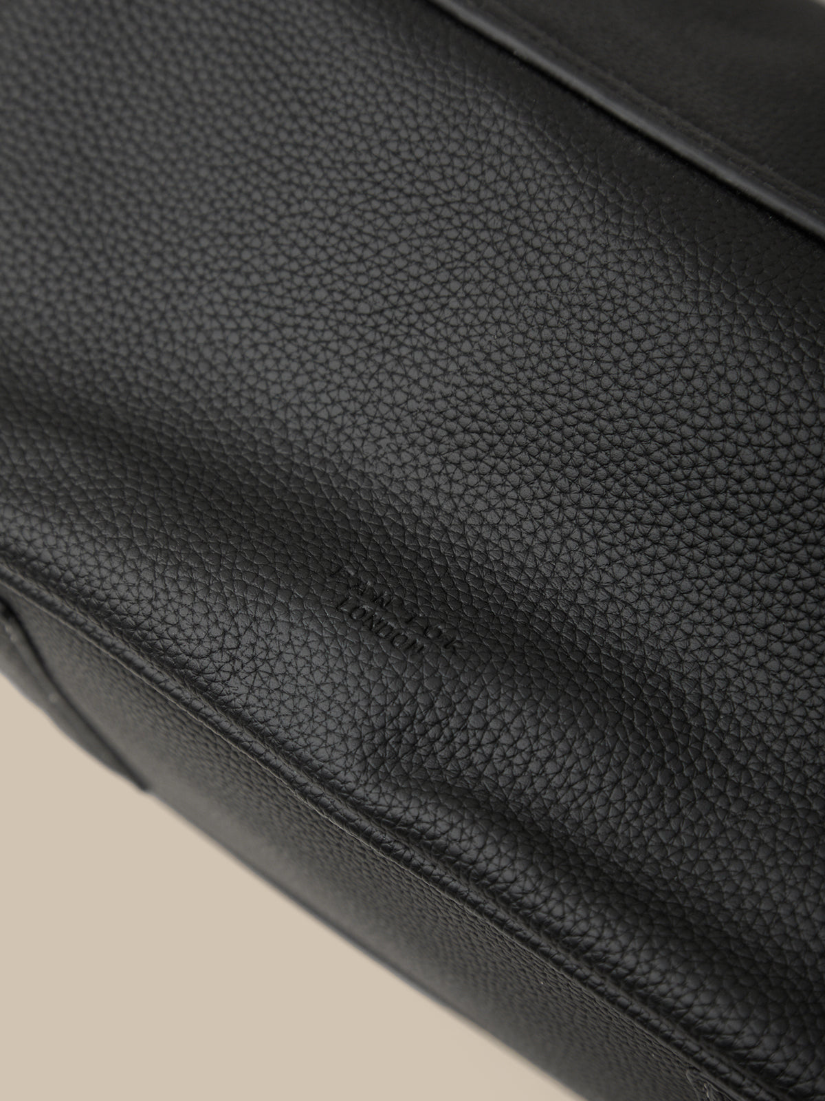 Close-up of a black leather bag with visible texture on a beige background