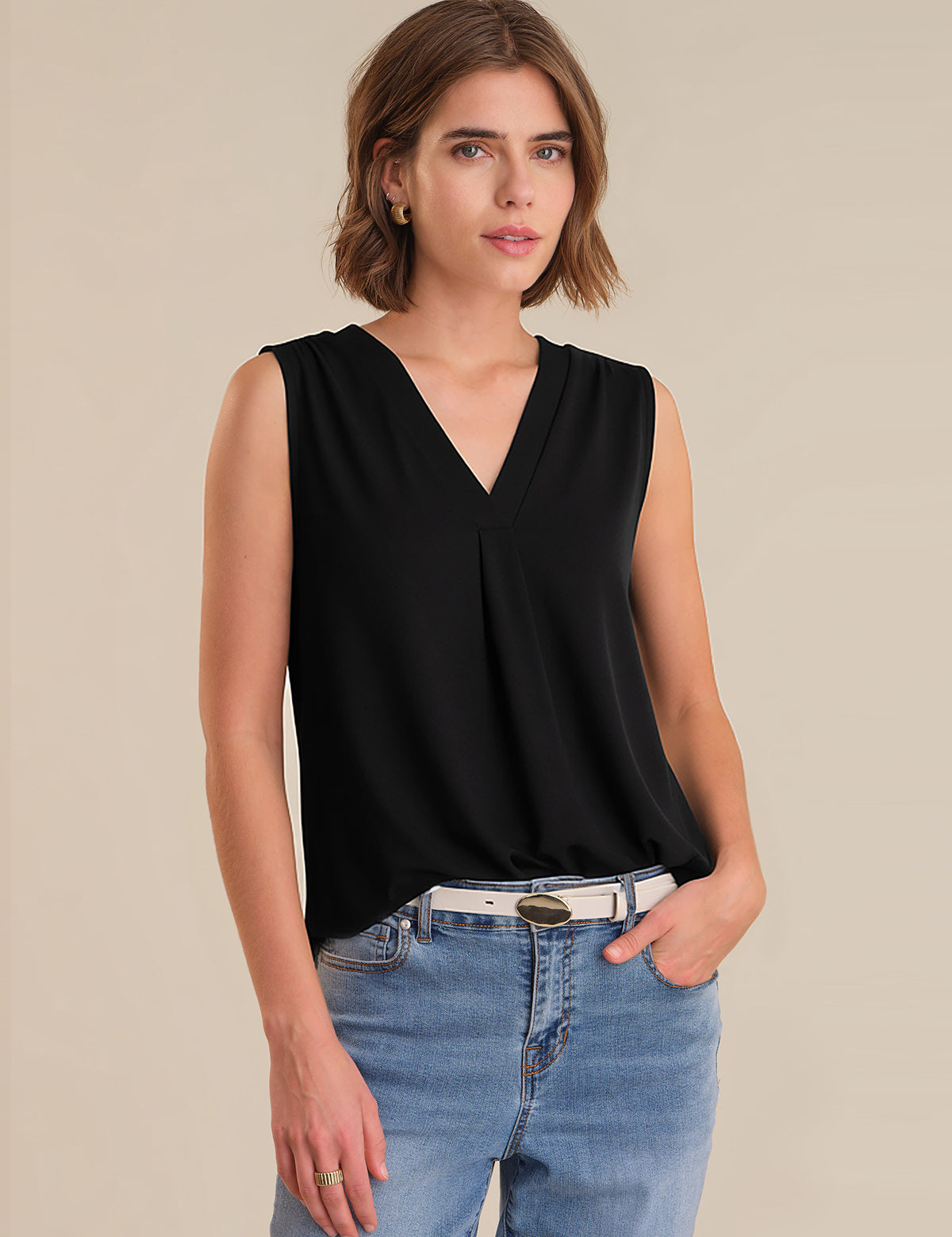Woman wearing a black sleeveless top and blue jeans on a beige background