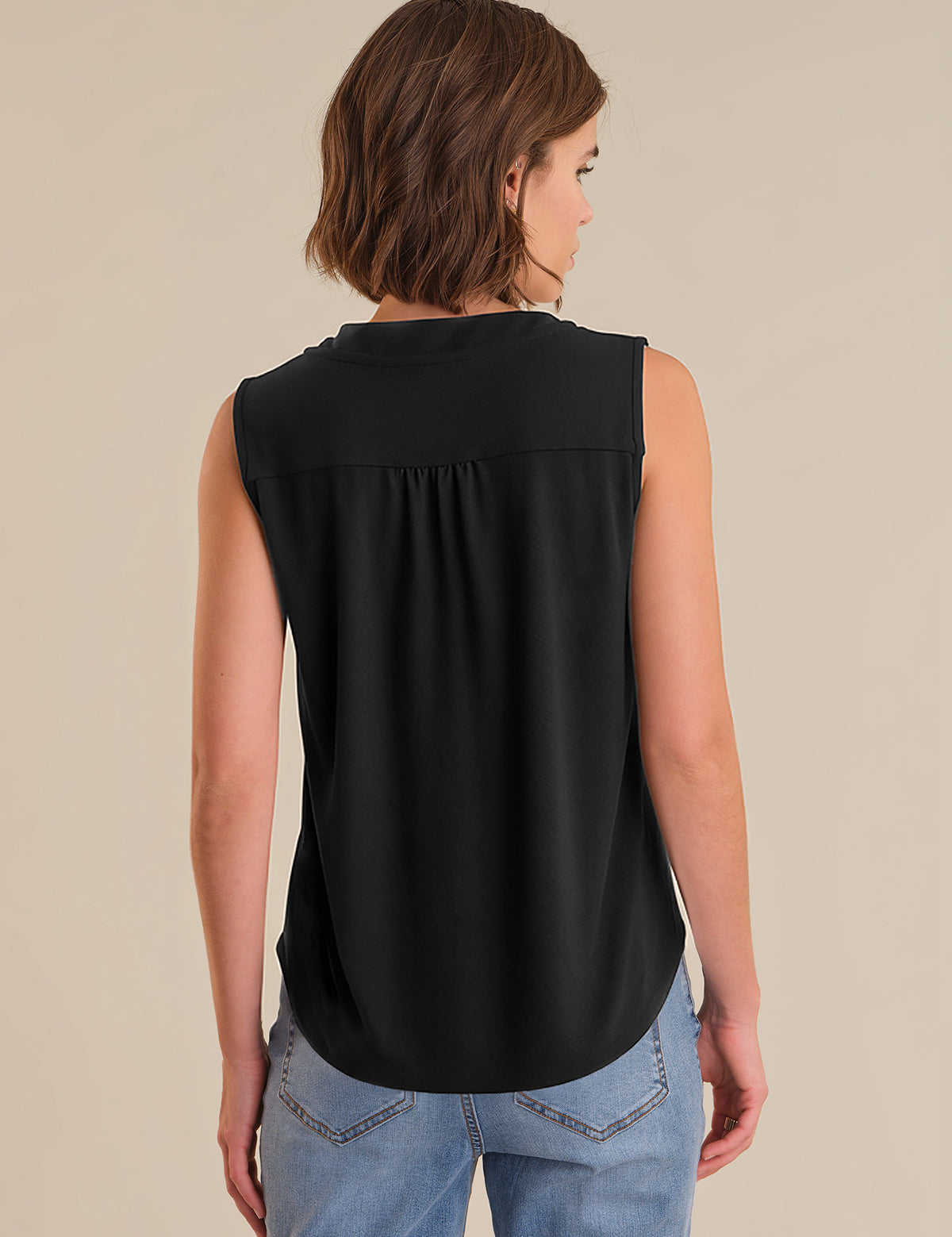 Woman wearing a black sleeveless top and blue jeans on a beige background