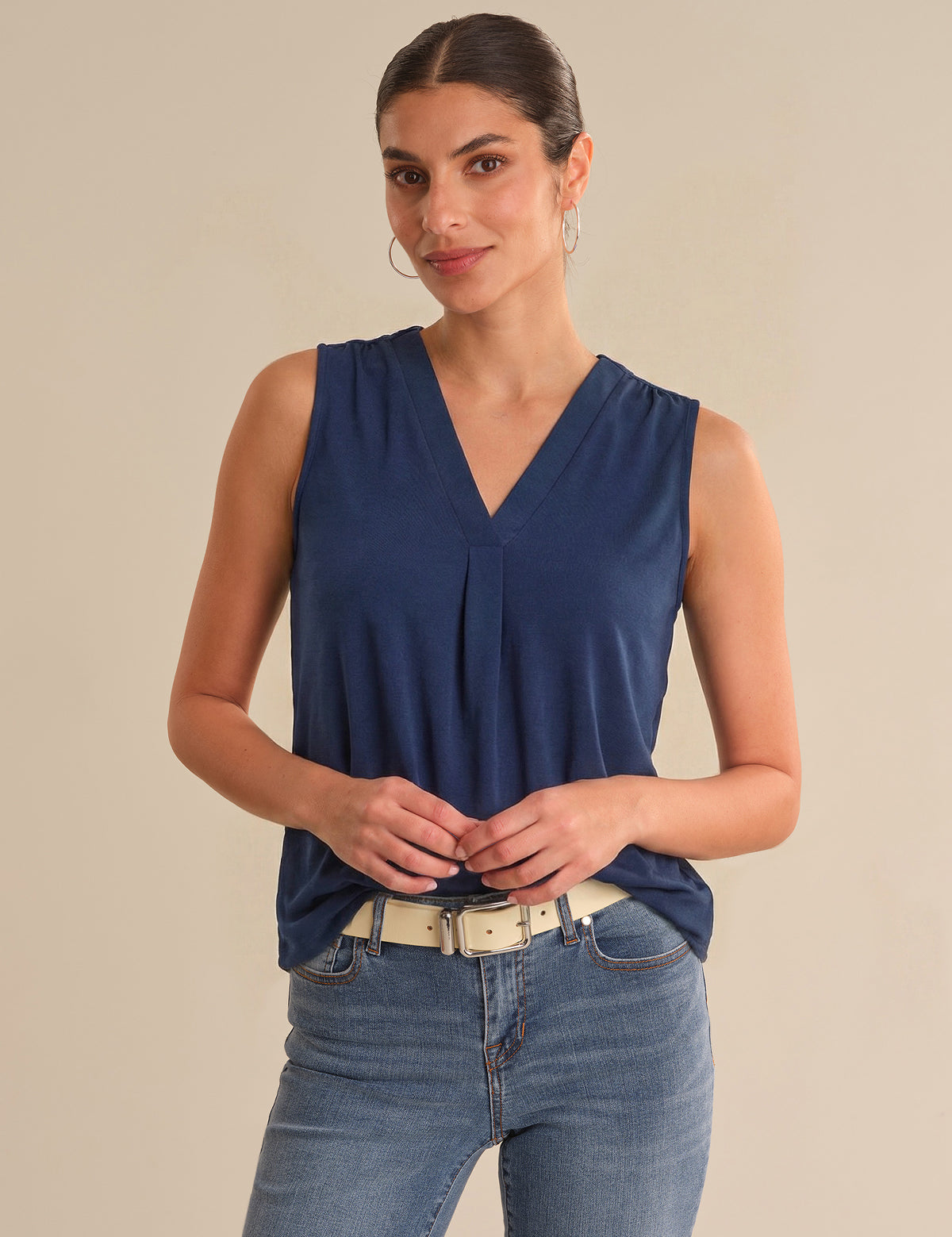 Woman wearing a blue sleeveless top and jeans on a beige background