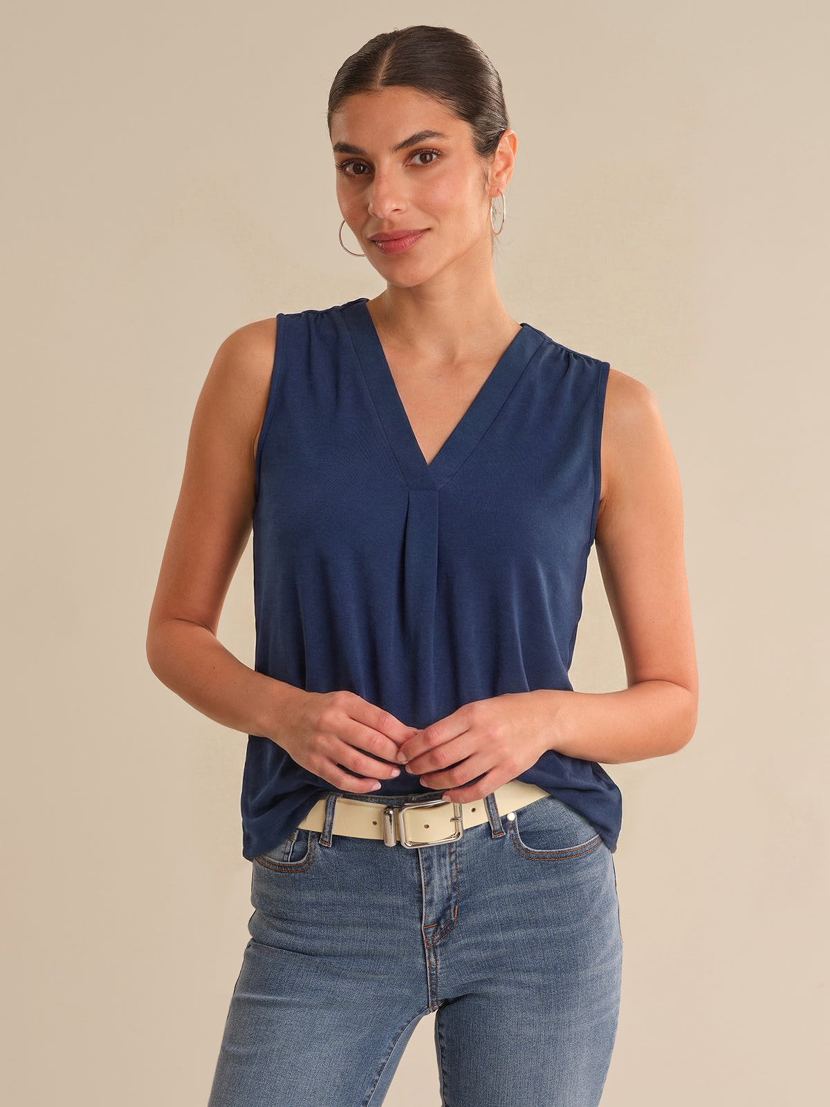 Woman wearing a blue sleeveless top and jeans on a beige background