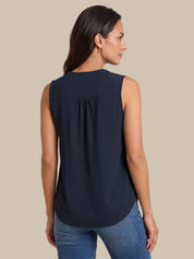 A woman shown from the back wearing a sleeveless navy blue blouse with a gathered back detail, paired with blue jeans, against a solid beige background.