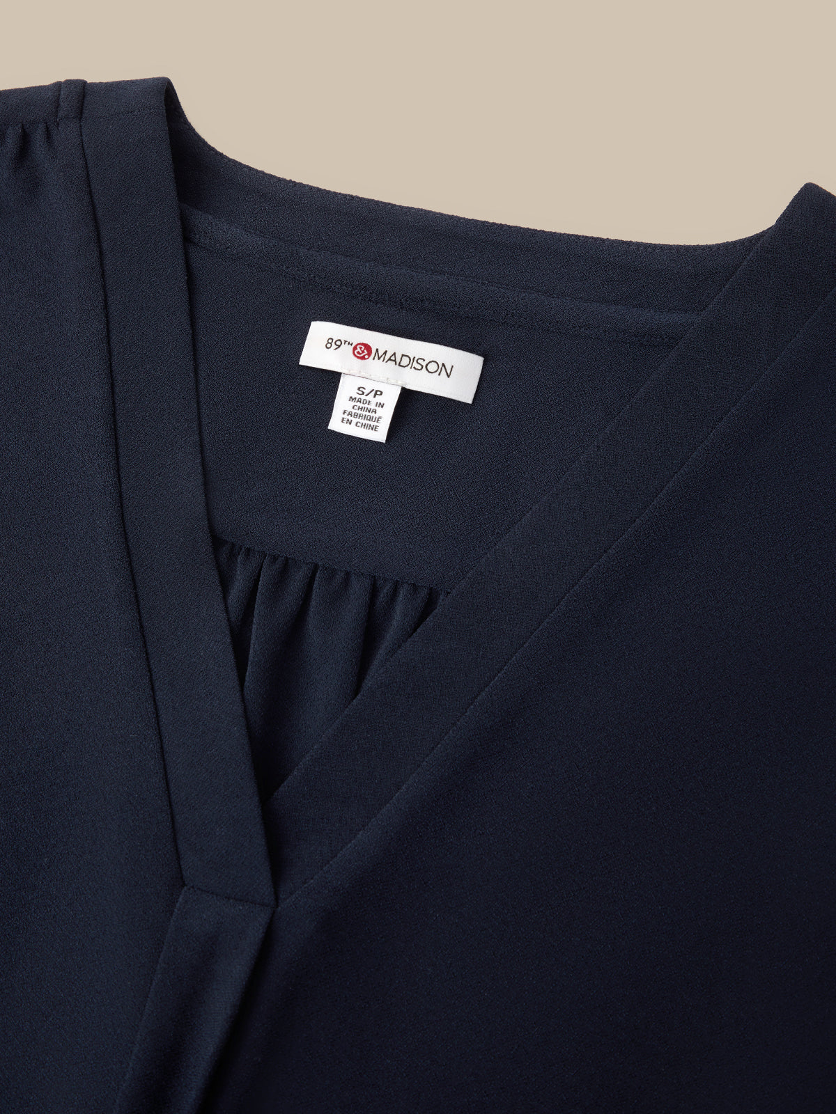 Close-up of a navy blue wrap-style top or dress with a gathered neckline and a visible white interior neck label reading 89 Madison.