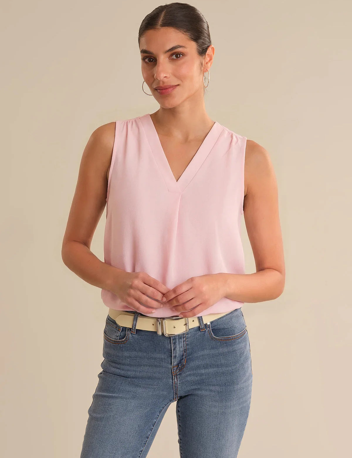 Woman wearing a pink sleeveless top and blue jeans on a beige background