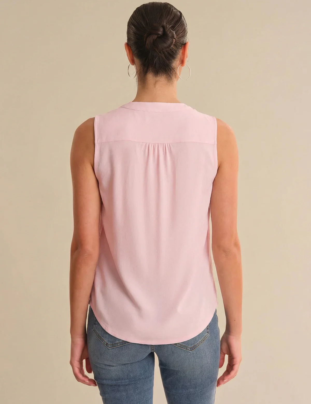 Person wearing a pink sleeveless top and blue jeans on a beige background