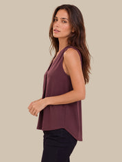 A woman wearing a sleeveless, v-neck top in a muted plum purple, paired with black pants, photographed against a solid beige background.