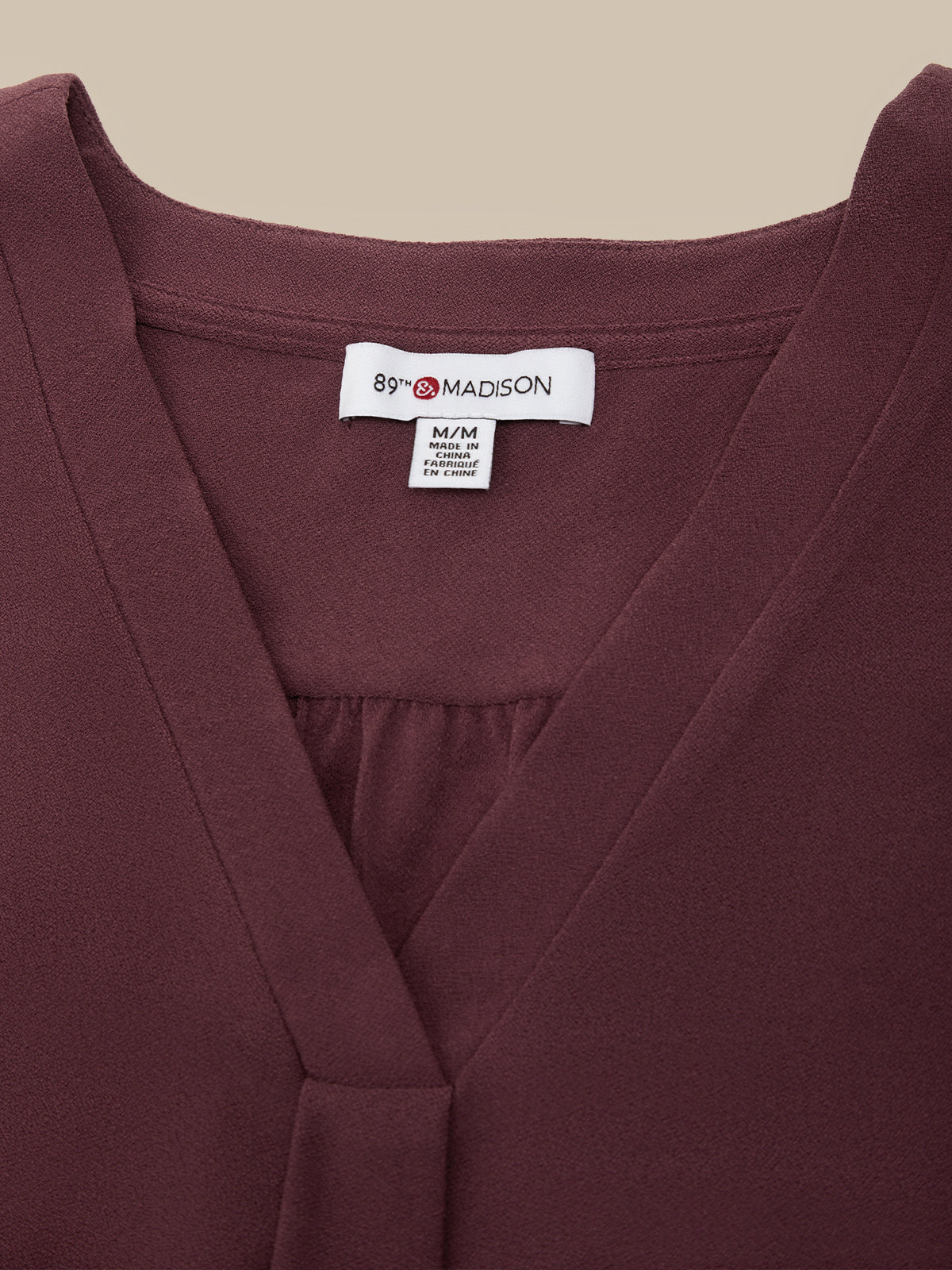 Close-up of a burgundy wrap-style top with a V-neckline and a visible white neck label reading 89 MADISON.