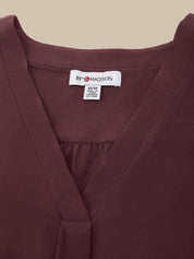Close-up of a burgundy wrap-style top with a V-neckline and a visible white neck label reading 89 MADISON.