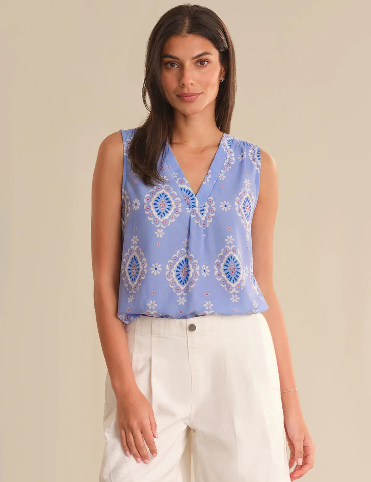 Woman wearing a blue patterned sleeveless top with white pants on a beige background