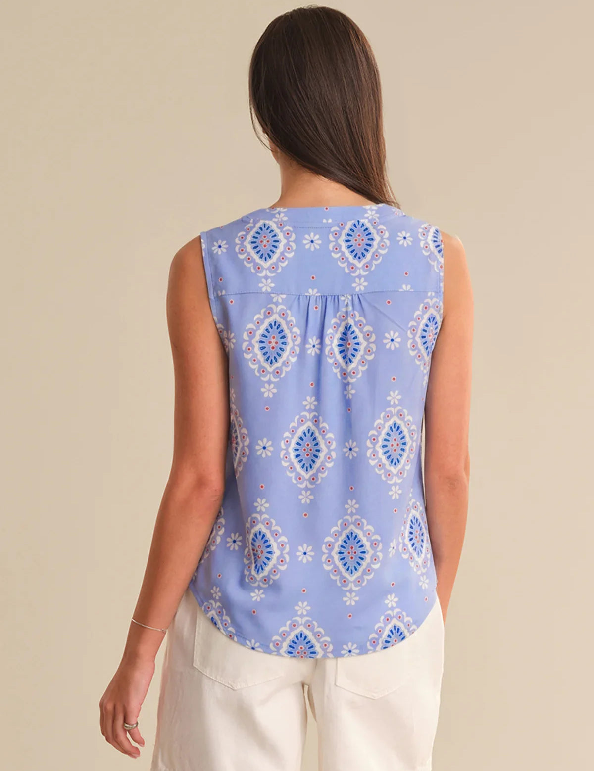 Woman wearing a sleeveless blue patterned top against a beige background