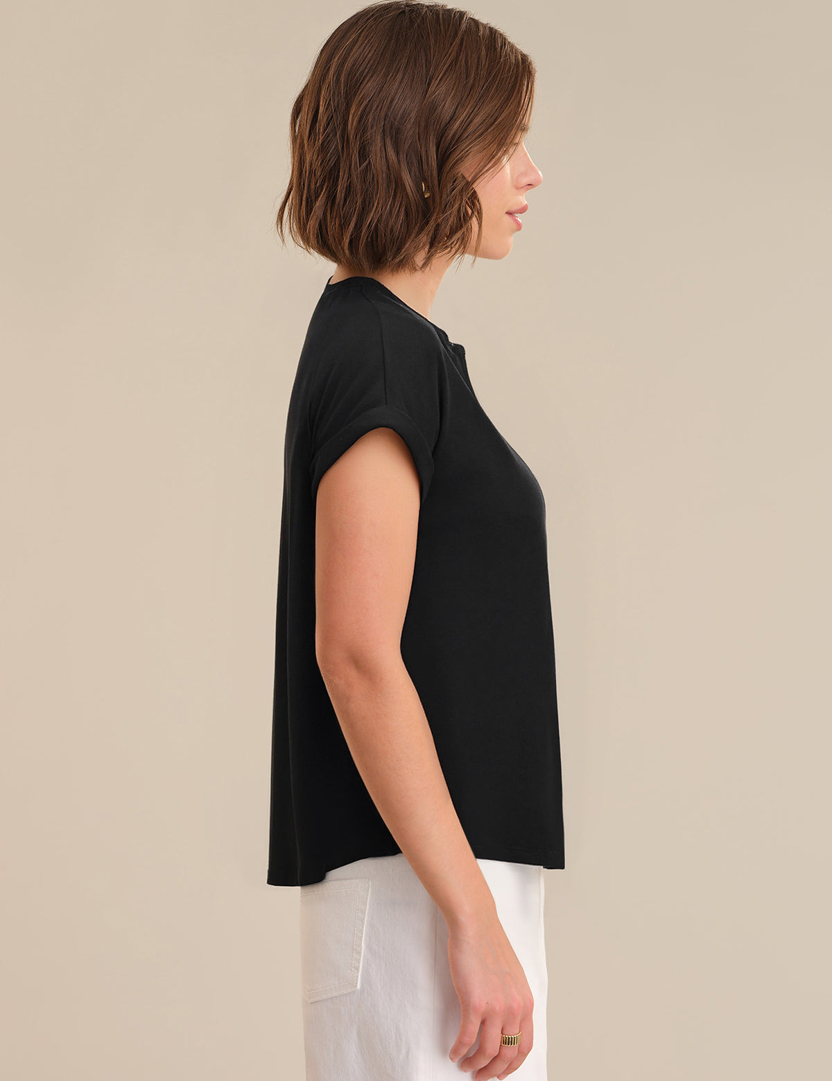 Woman wearing a black top and white pants against a beige background