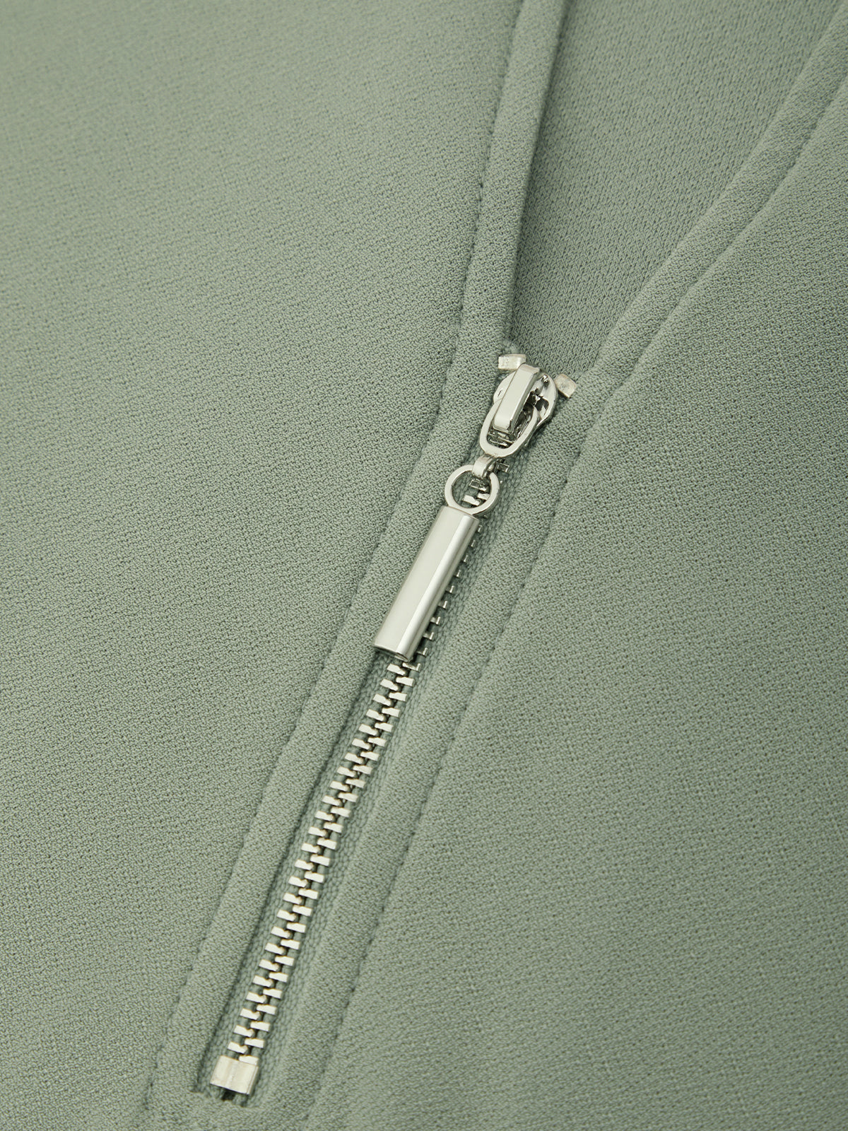 Close-up of a sage green zippered garment with a silver metal zipper pull.