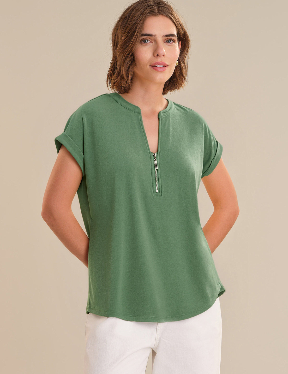 Woman wearing a green short-sleeve top with a zipper on a beige background