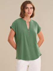 Woman wearing a green short-sleeve top with a zipper on a beige background