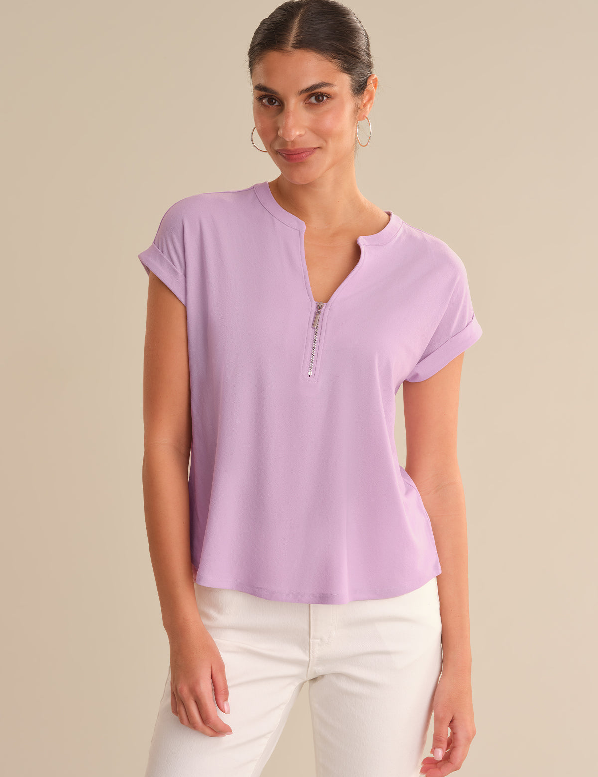 Woman wearing a light purple short-sleeve top with a zipper on a beige background