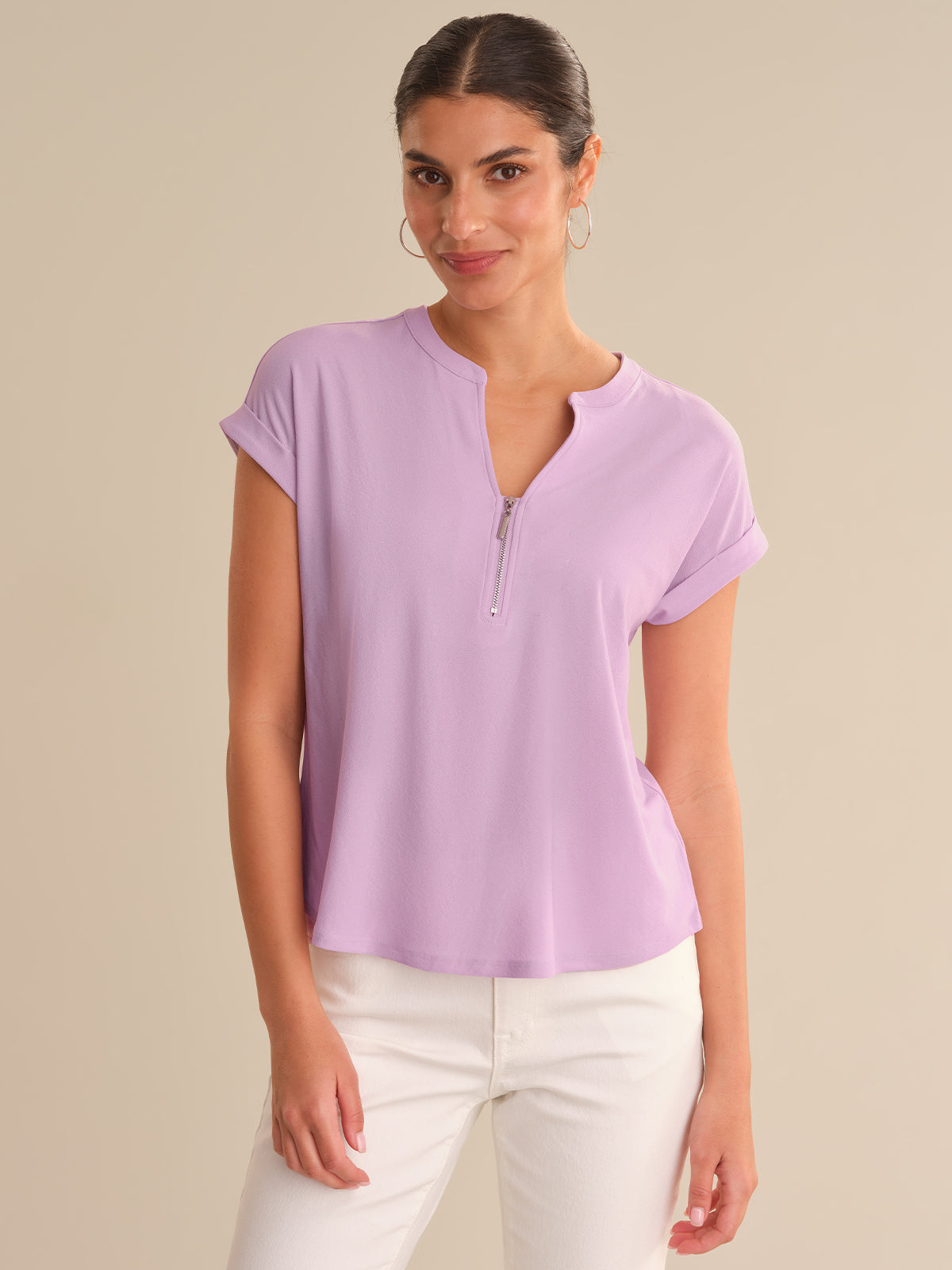 Woman wearing a light purple short-sleeve top with a zipper on a beige background