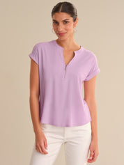Woman wearing a light purple short-sleeve top with a zipper on a beige background