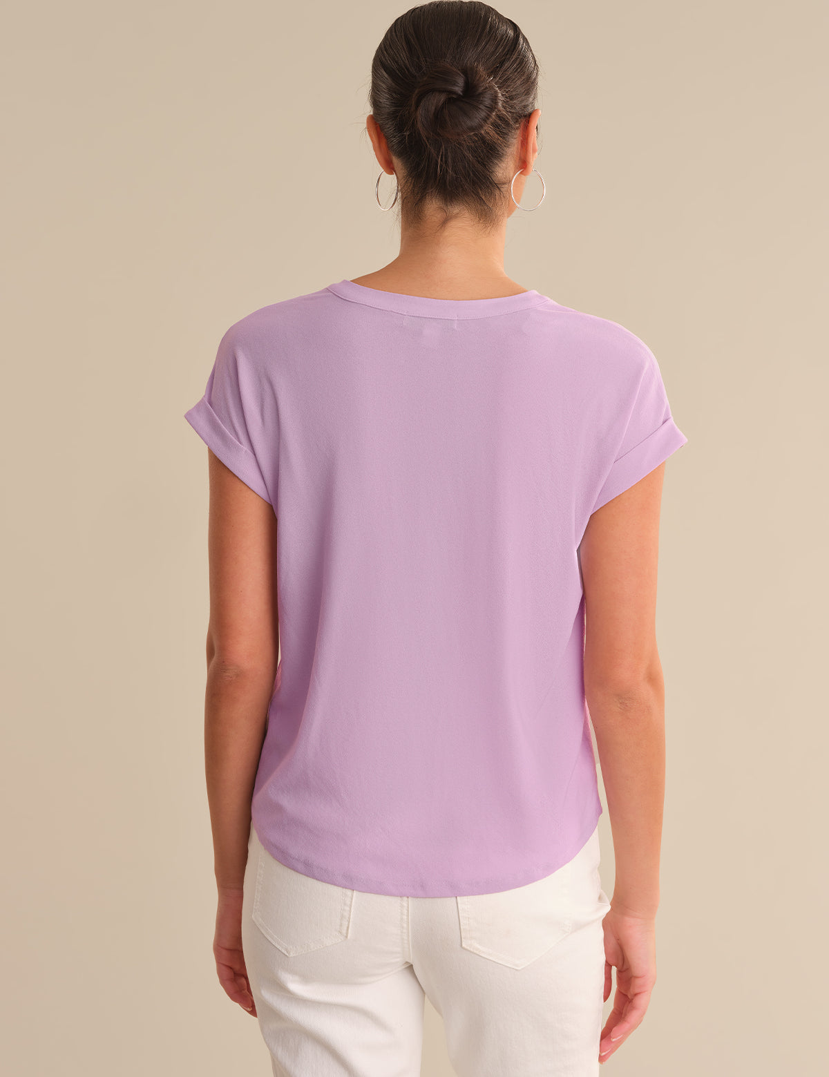 Person wearing a purple t-shirt and white pants on a beige background