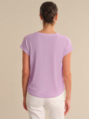 Person wearing a purple t-shirt and white pants on a beige background