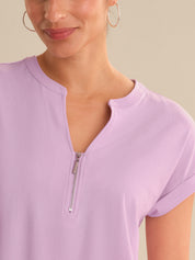 Close-up of a person wearing a light purple short-sleeve top with a zipper detail on a neutral background