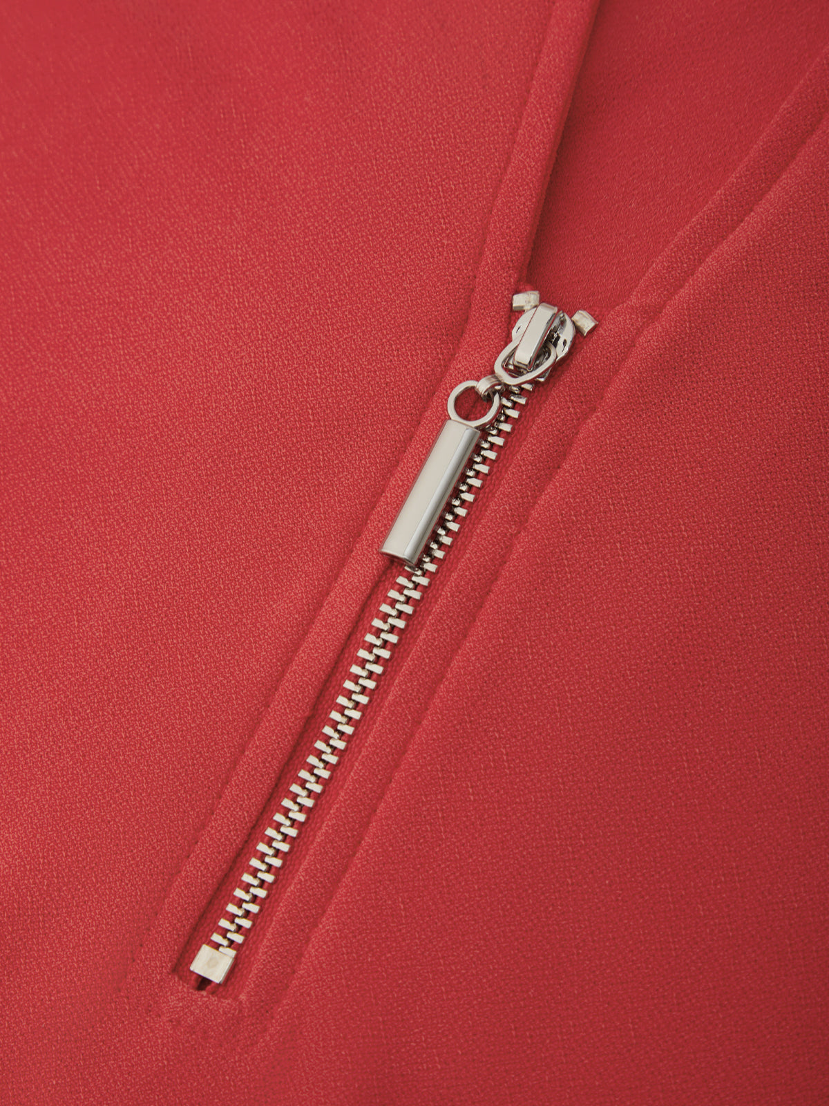 Close-up of a red garment featuring a silver metal zipper with a rectangular pull tab.