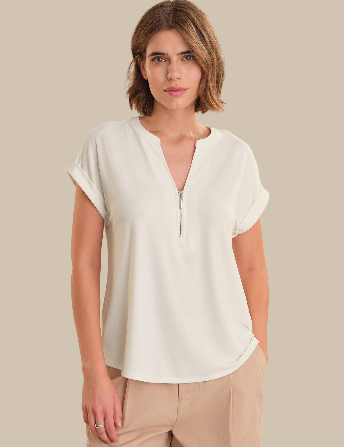 Woman wearing a white blouse with a zipper on a beige background