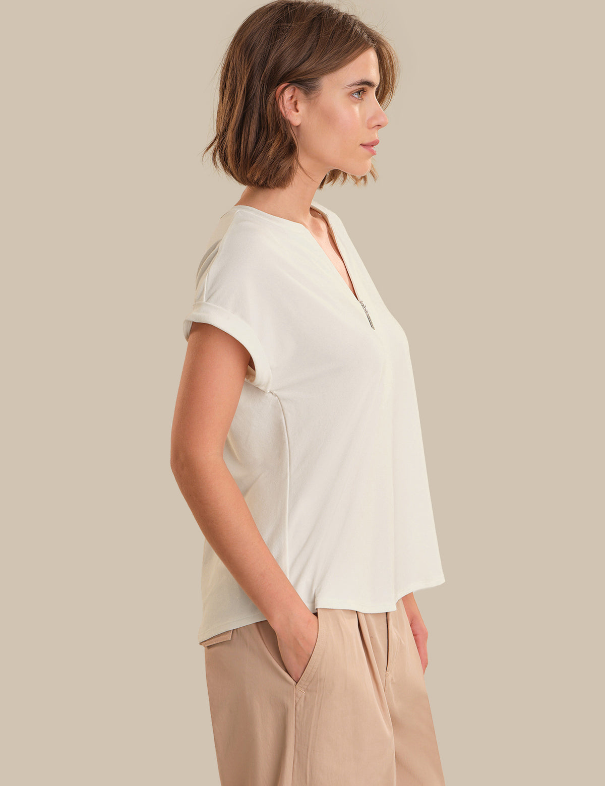 Woman wearing a white blouse and beige pants against a plain background