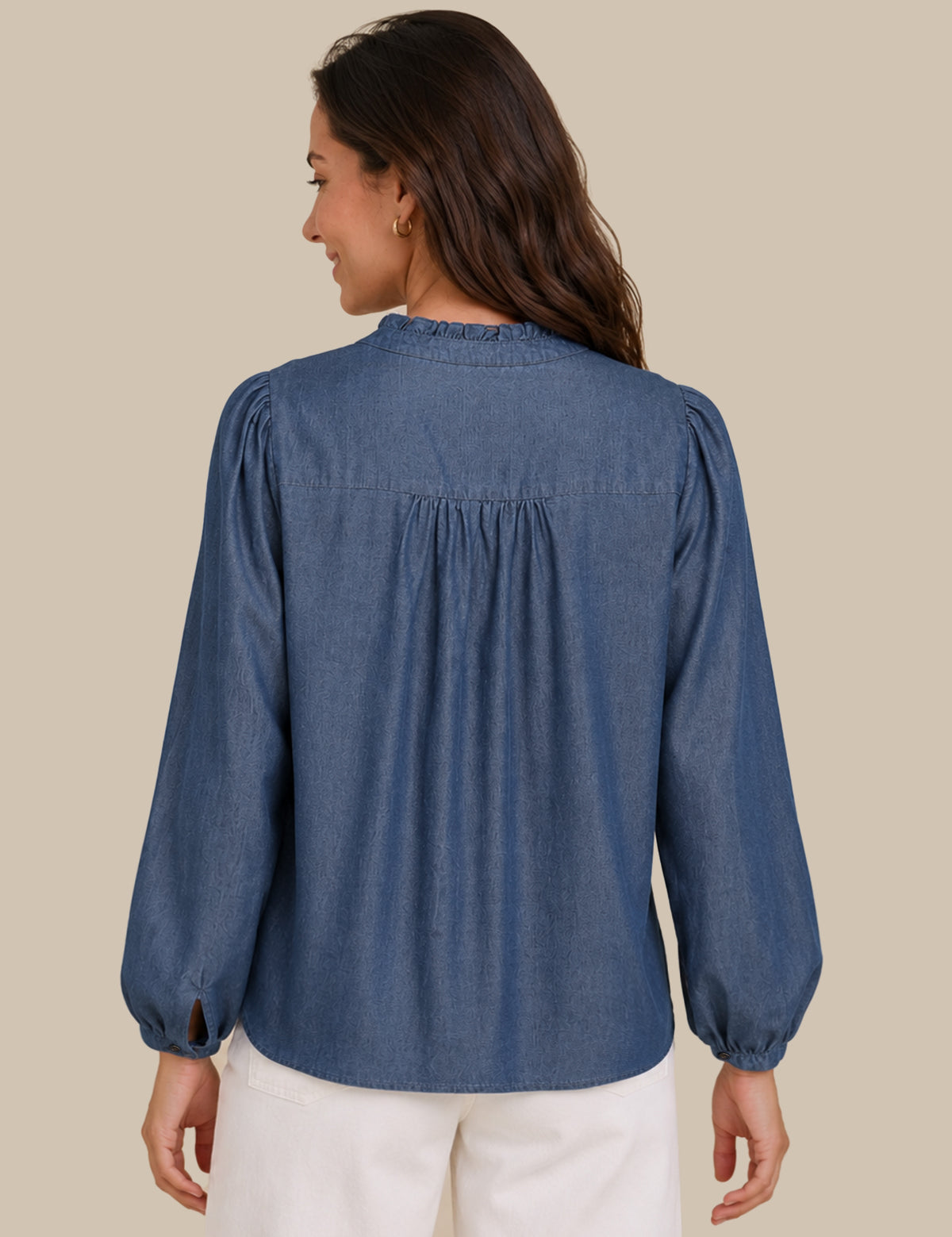 A woman shown from the back wearing a dusty blue long-sleeve blouse with a gathered, pleated back and white pants, set against a solid beige background.