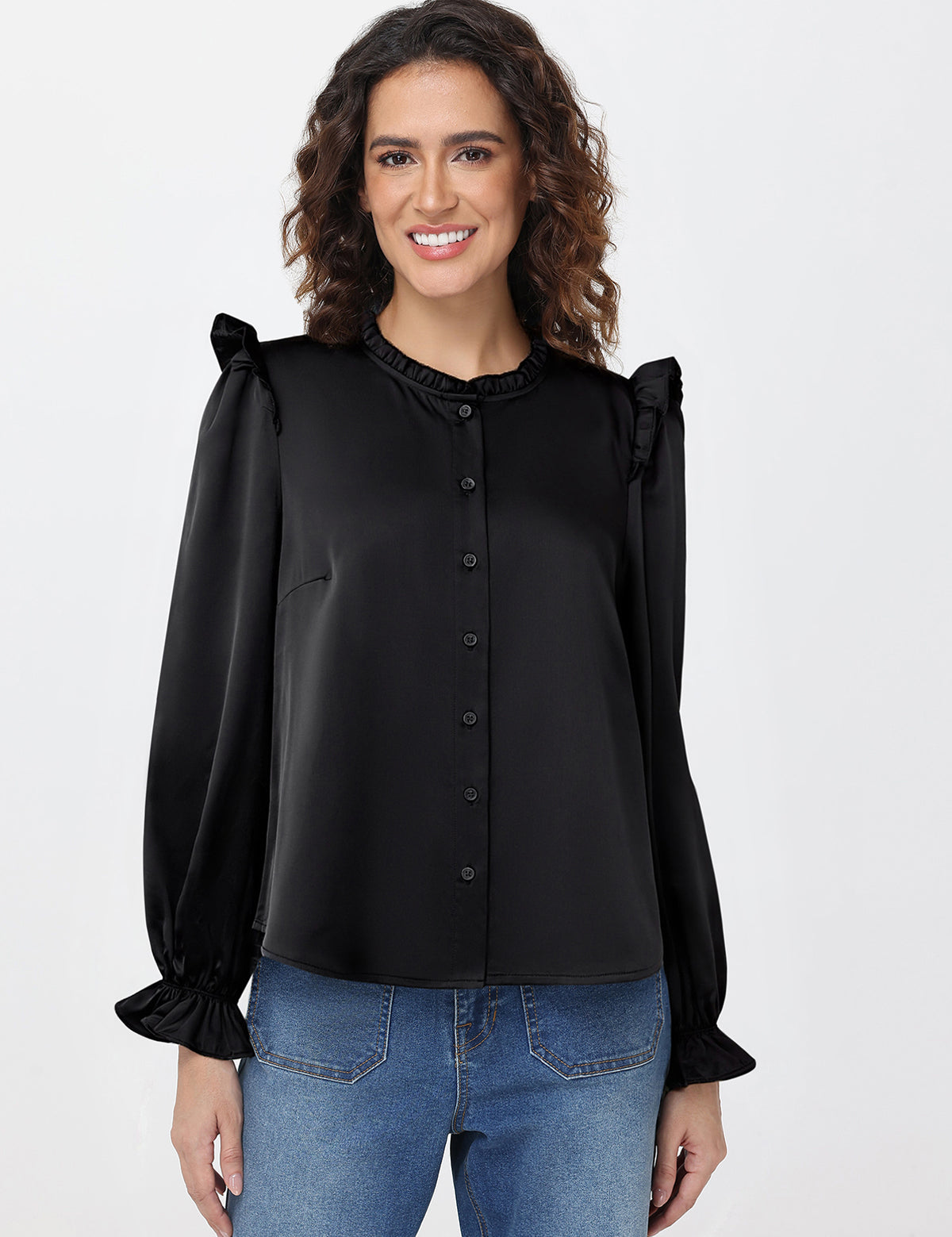 Woman wearing a black blouse with ruffled sleeves and blue jeans on a white background