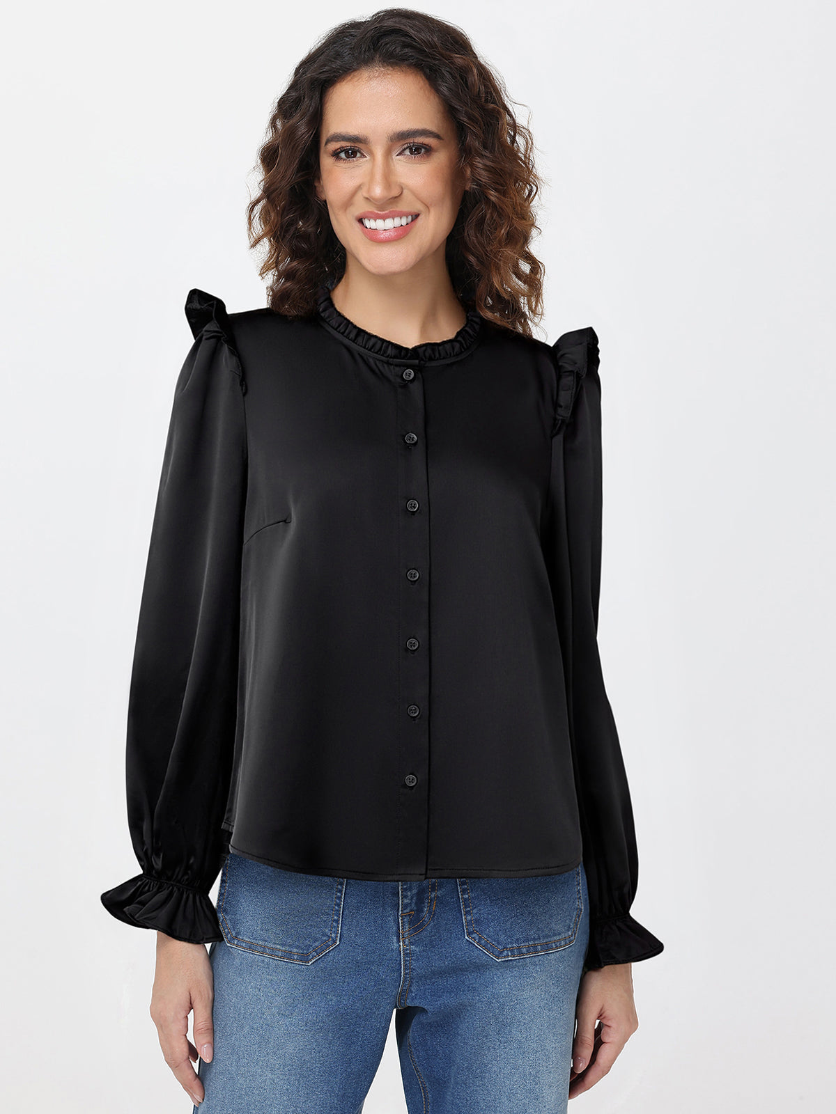 Woman wearing a black blouse with ruffled sleeves and blue jeans on a white background