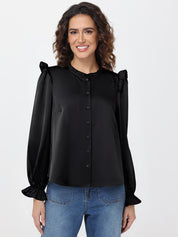 Woman wearing a black blouse with ruffled sleeves and blue jeans on a white background