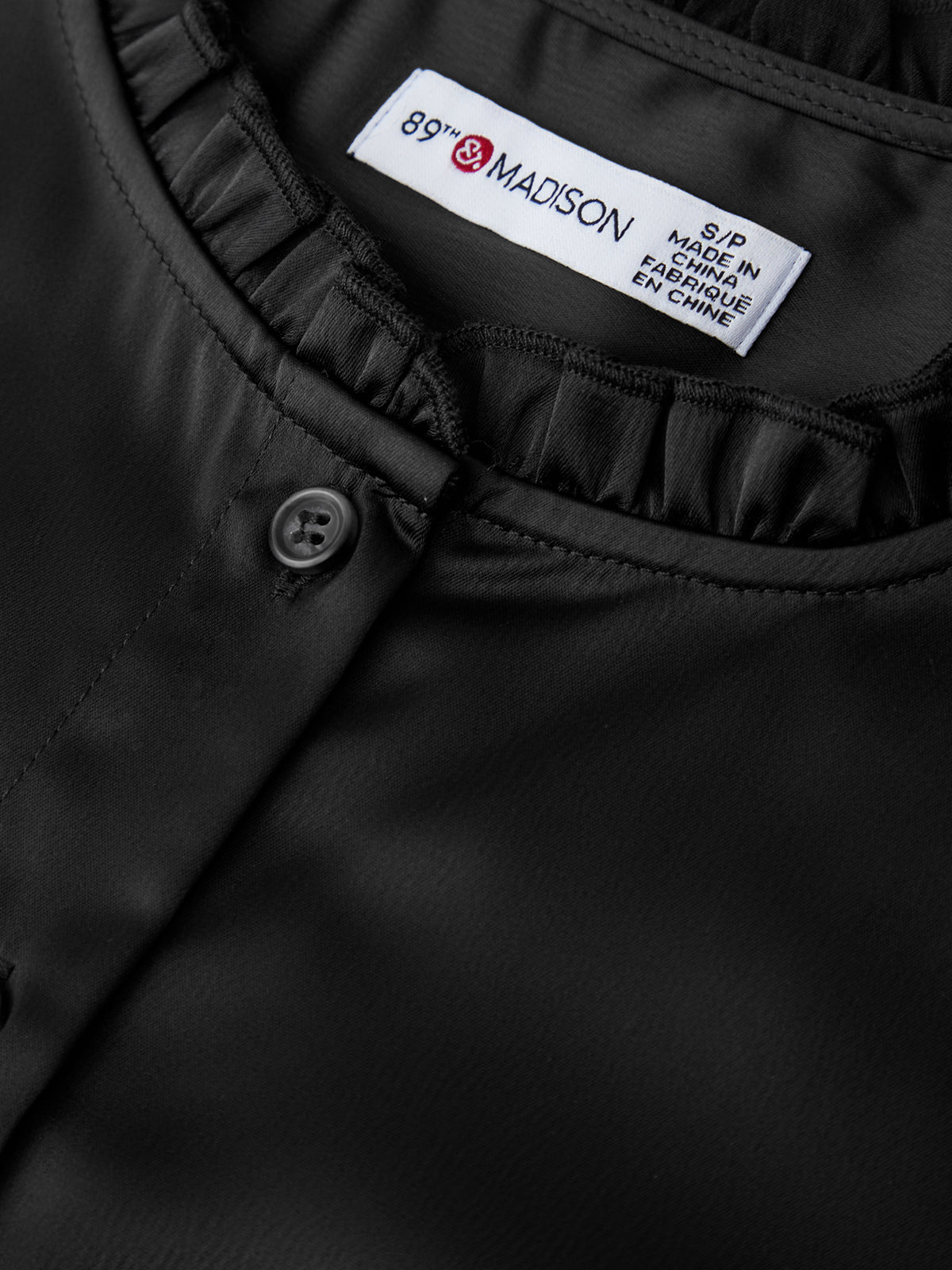 Close-up of a black garment with a 'Madison' label on a dark background