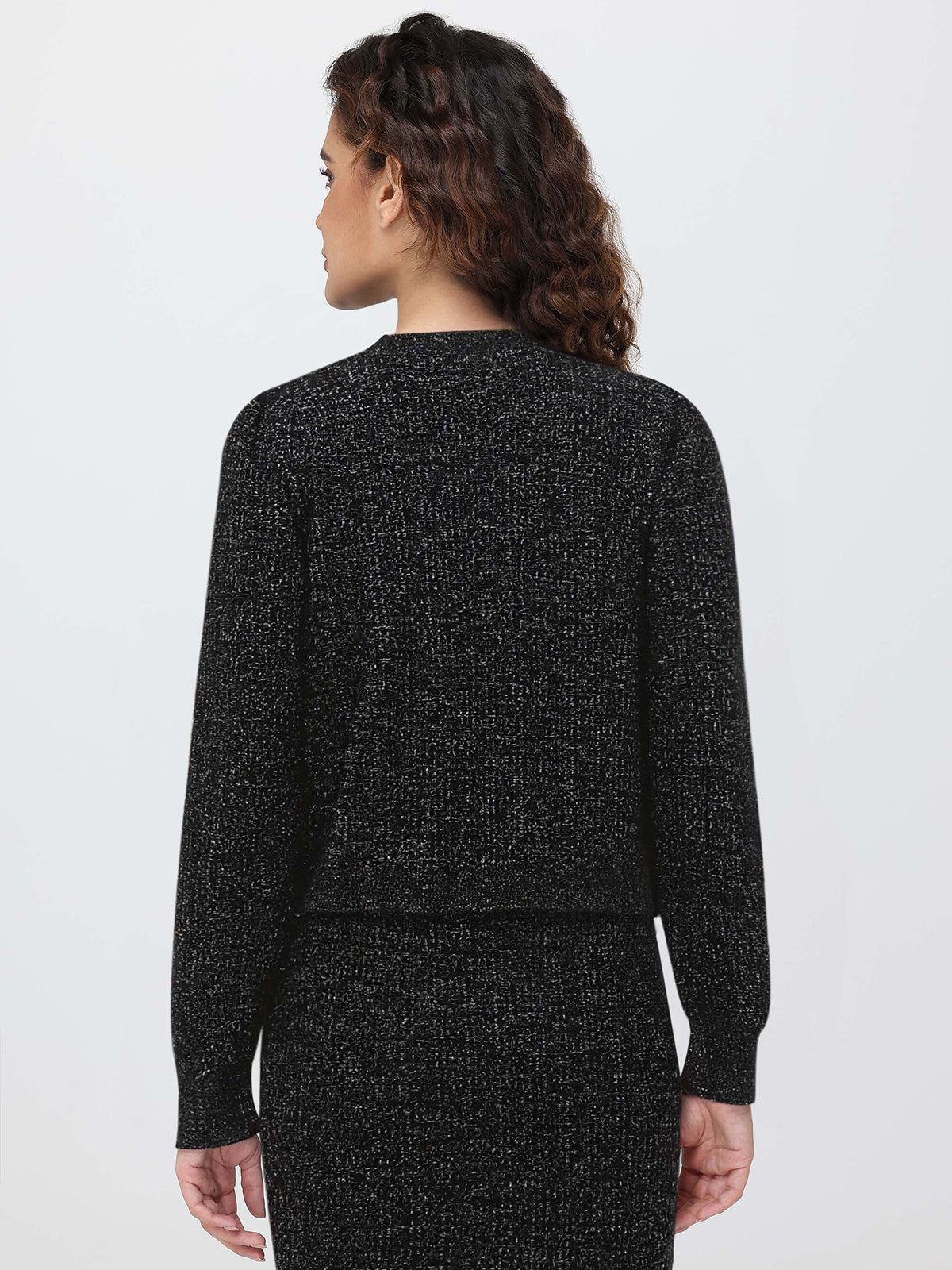 Person wearing a black textured cardigan and skirt set on a light gray background