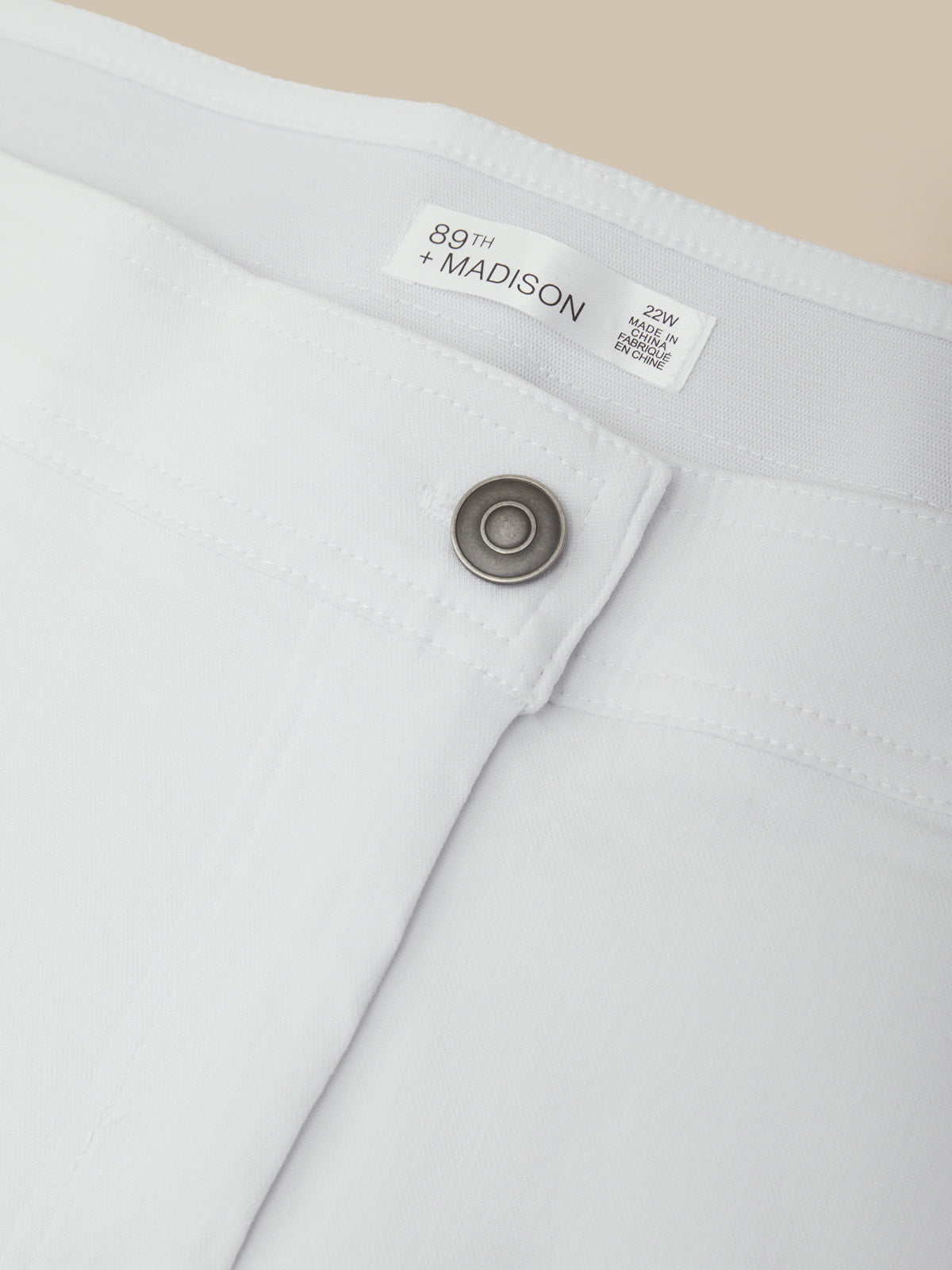 Close-up of a white pants pocket with a button and '89th Madison' label on a beige background