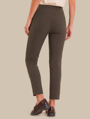 A person shown from the back wearing slim-fit cropped trousers in a dark olive brown color, paired with dark brown leather loafers, against a solid beige background.
