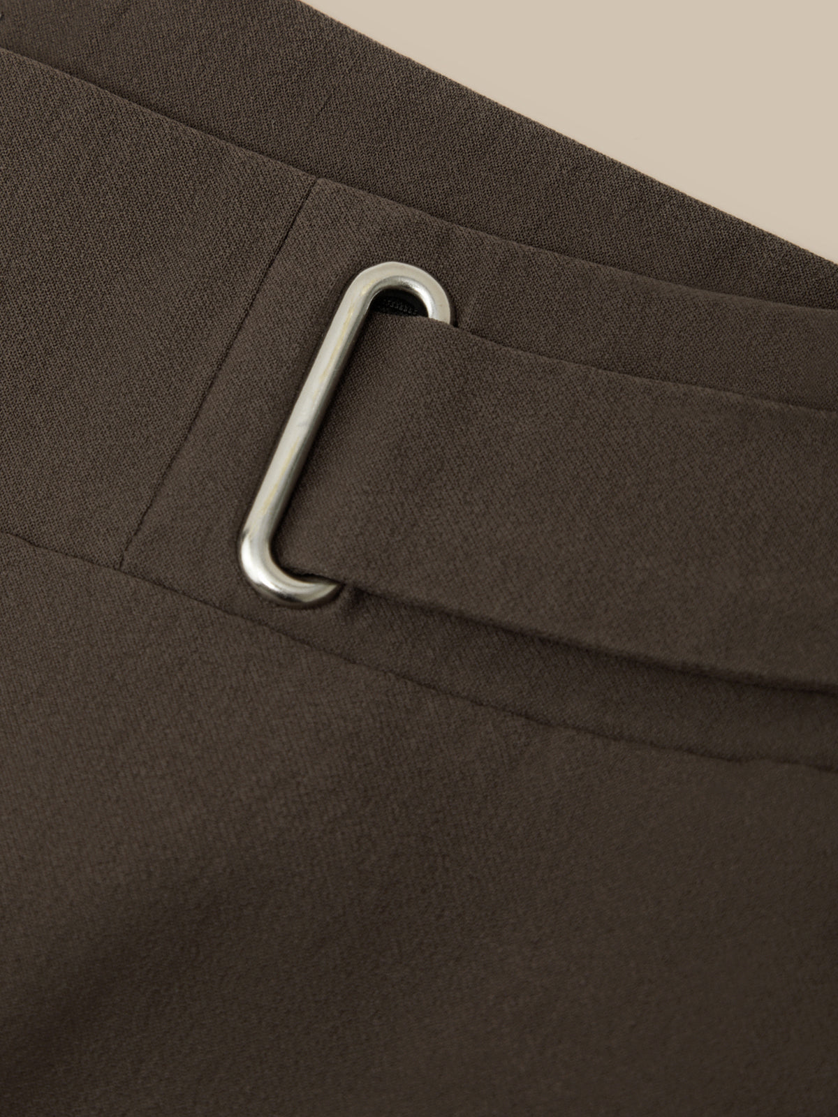 Close-up of a dark brown fabric belt with a silver-toned metal buckle on a matching belt loop.