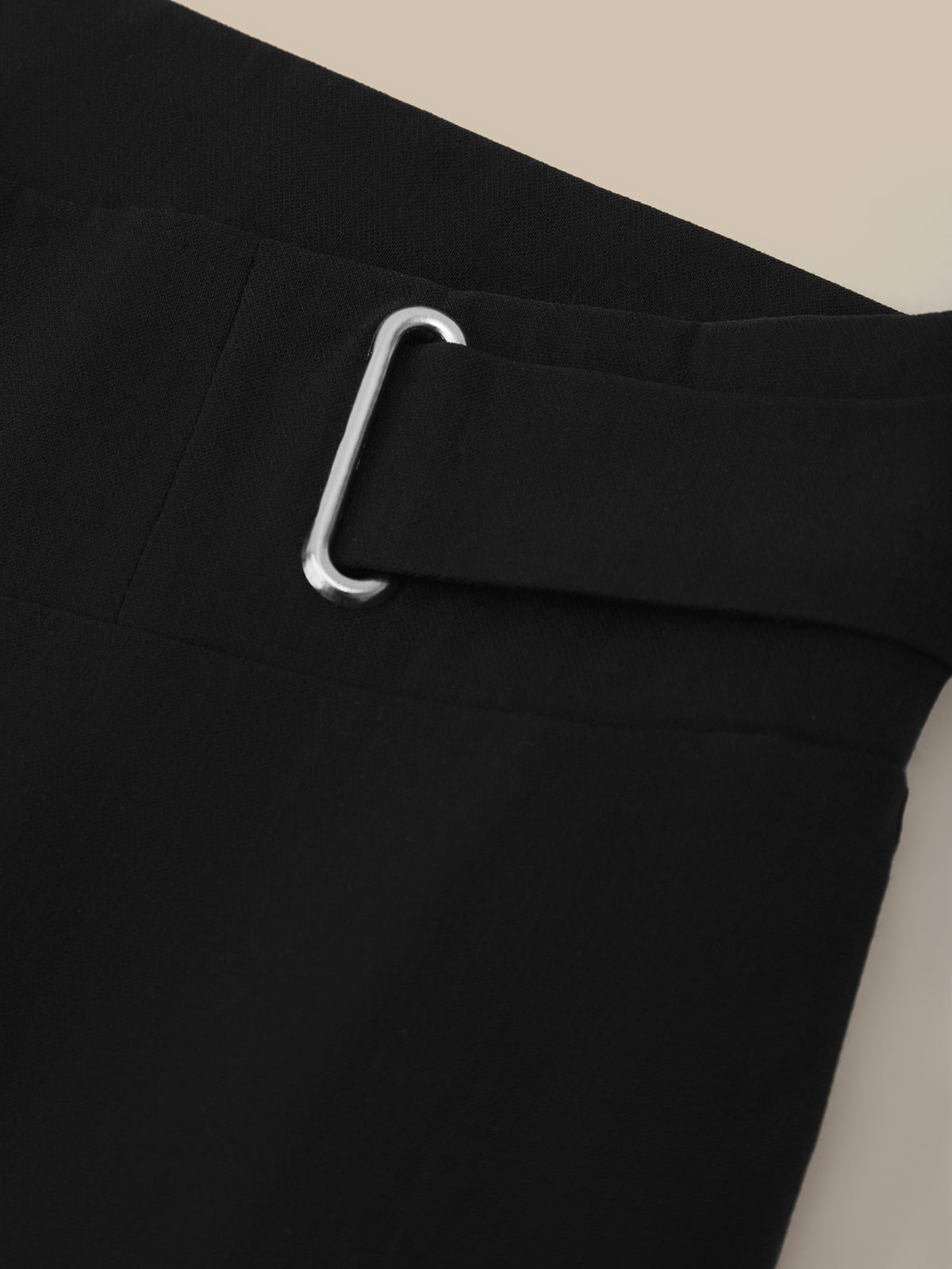Close-up of a black pants with a silver buckle on a beige background