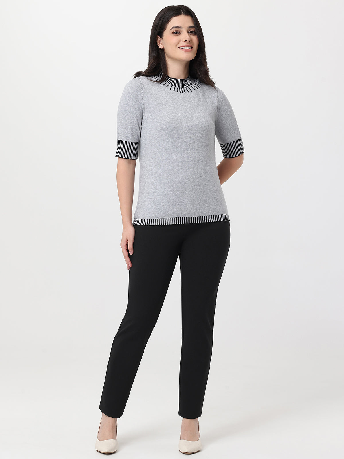 Woman wearing a gray sweater with black trim and black pants on a white background
