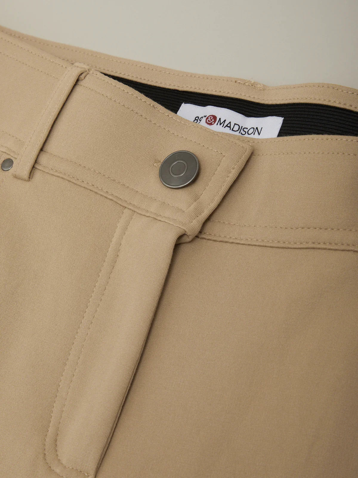 Close-up of beige pants with a brand label on a neutral background