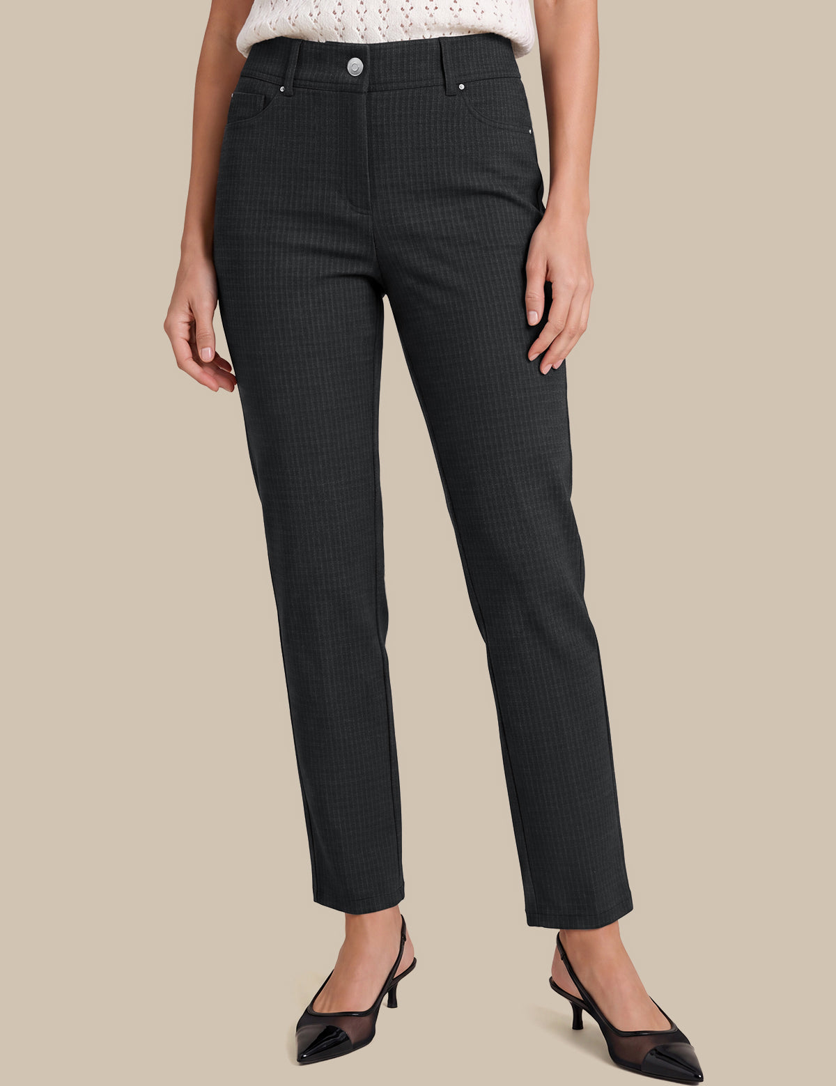 A model wearing a pair of dark charcoal gray slim-fit trousers with a subtle micro-check pattern, styled with a white knit top and black slingback heels against a solid beige background.
