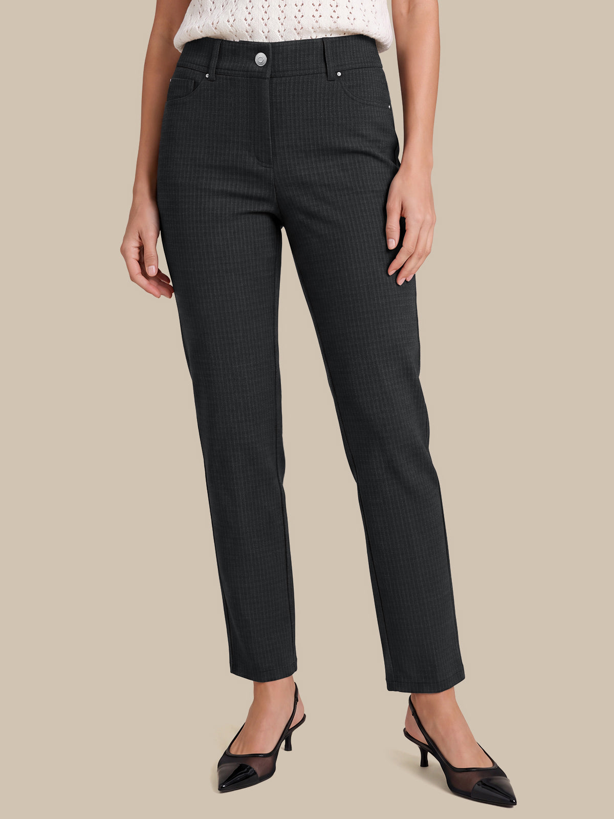 A model wearing a pair of dark charcoal gray slim-fit trousers with a subtle micro-check pattern, styled with a white knit top and black slingback heels against a solid beige background.