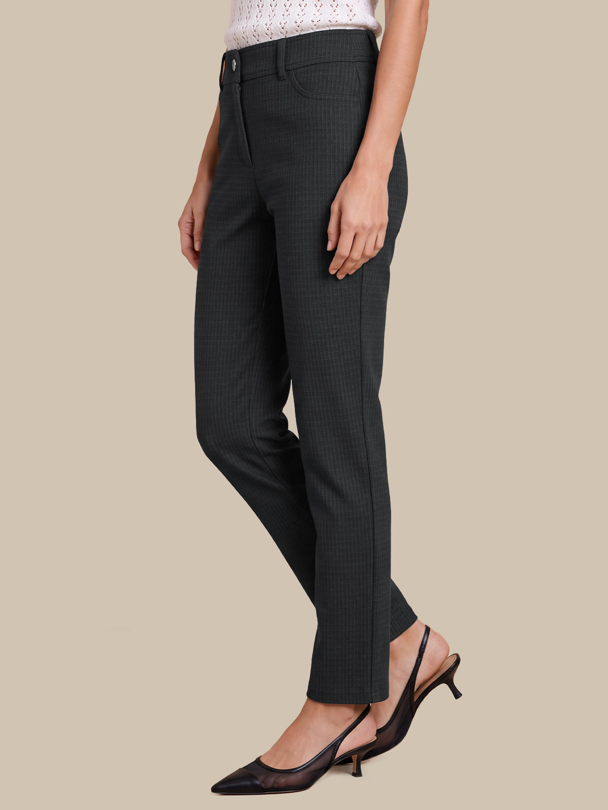 A model wearing dark charcoal gray micro-check trousers, styled with a white top and black slingback kitten heels, set against a solid beige background.