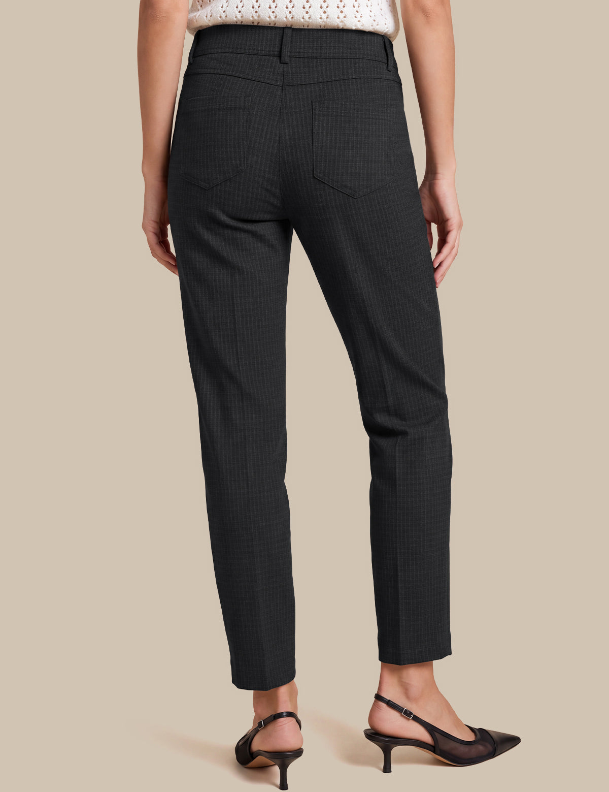 A model shown from the back wearing black cropped trousers with a subtle micro-check pattern, paired with black slingback heels and a white knit top, set against a solid beige background.