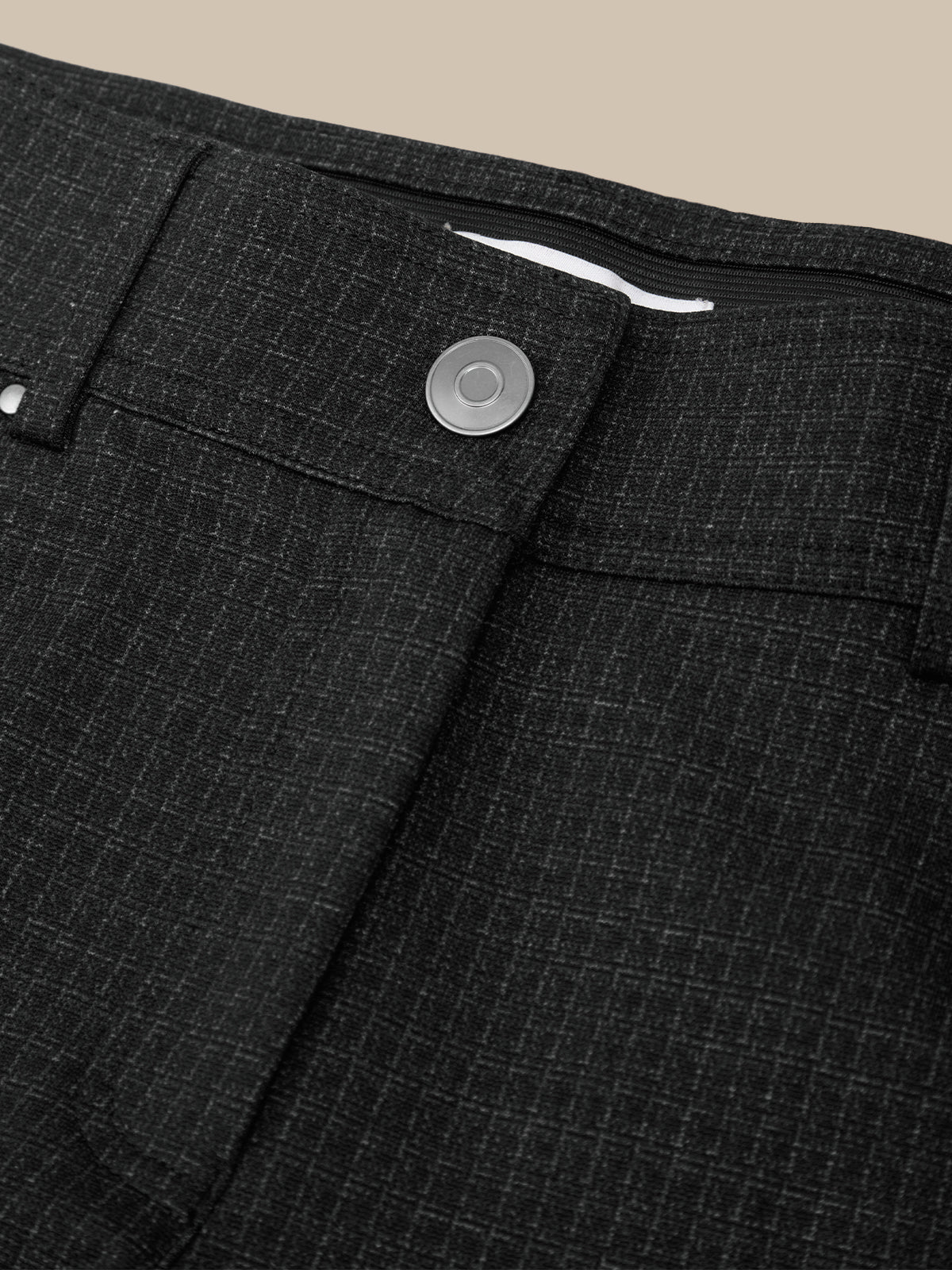 Close-up of dark charcoal gray textured trousers showing the waistband, button closure, and fabric weave against a beige background.